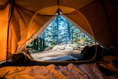 Luxury glamping tent with comfortable furnishings illuminated by warm golden light at sunrise in a scenic wilderness setting