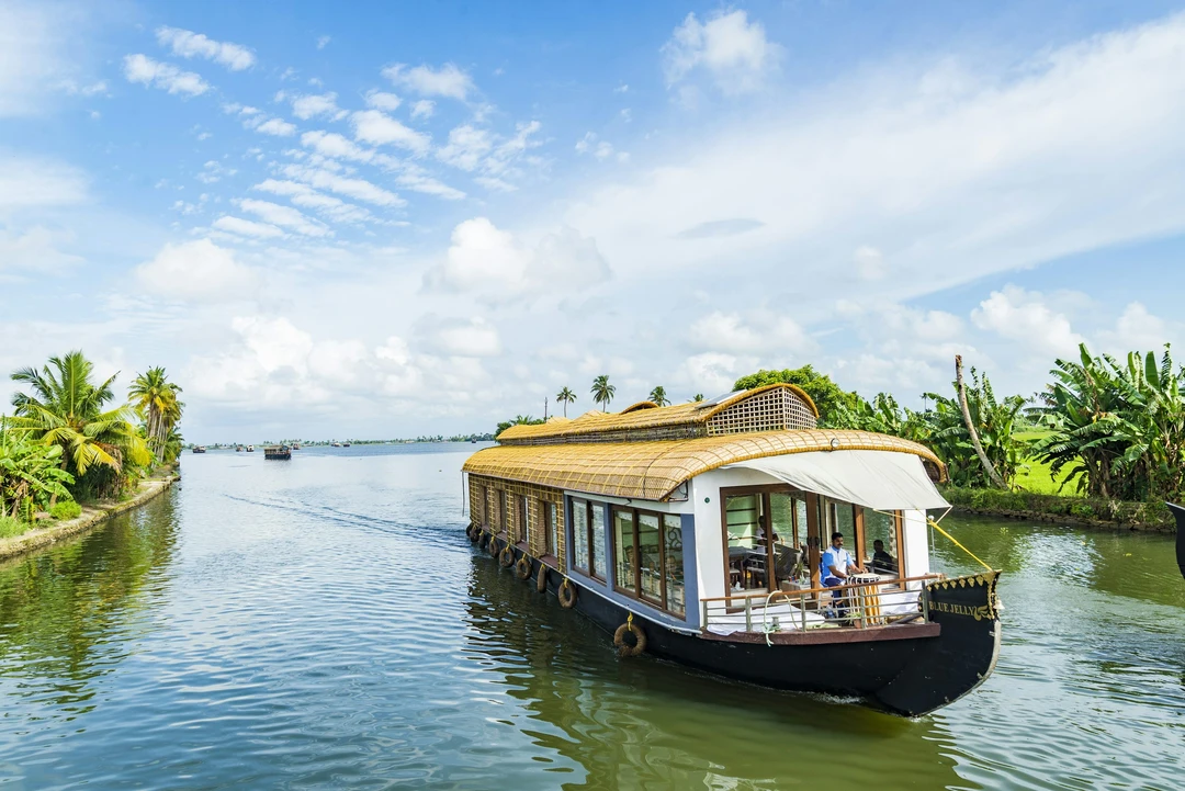 A traditional houseboat glides through a tranquil, palm-fringed canal in the beautiful backwaters of Alleppey, Kerala