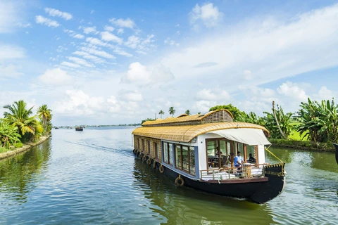 A Serene Houseboat Cruise on the Kerala Backwaters A traditional houseboat glides through a tranquil, palm-fringed canal in the beautiful backwaters of Alleppey, Kerala