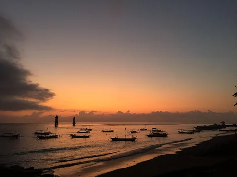 Bali First Timer: Temples, Terraces & Beach on a Smart Budget | Safari Sutra Holidays Kuta Beach Bali at golden hour — surfers catching waves with orange sky above, Bali budget tour India