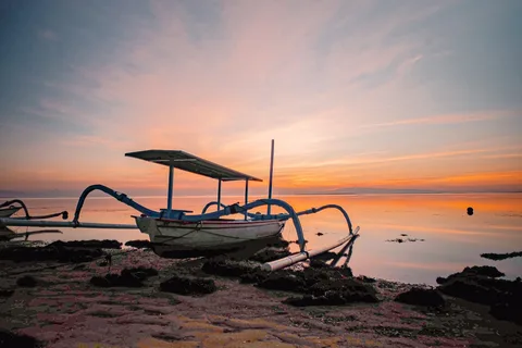 Bali at Your Pace: Temples, Highlands & Calm Shores for Seniors | Safari Sutra Holidays Sanur beach Bali at sunrise — calm reef-protected shoreline with traditional boats and morning light
