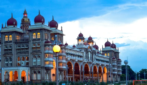 The Mysore Palace Illuminated at Dusk, Mysuru The grand facade of the Mysore Palace in Mysuru, beautifully illuminated with warm lights against a deep blue twilight sky
