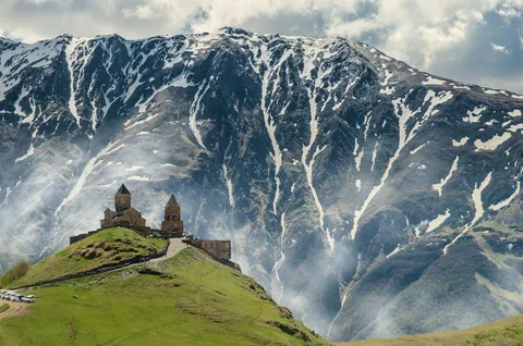 Three Capitals, One Mountain Range: The Caucasus Luxury Grand Tour | Safari Sutra Holidays Caucasus mountains and a hilltop church on a luxury Caucasus tour package from India