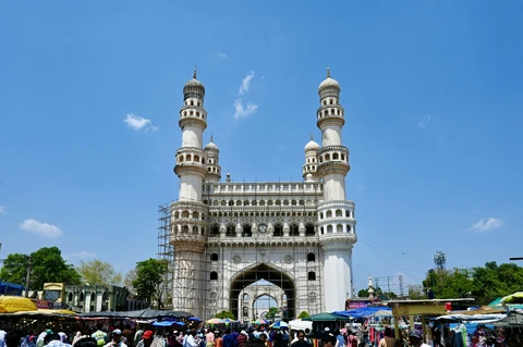 The Majestic Charminar of Hyderabad on a Sunny Day The magnificent Charminar monument, with its four grand minarets, rises above a colorful street market under a clear blue sky