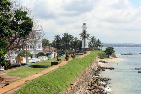 Tourists walk along the grassy ramparts of the colonial-era Galle Fort towards the iconic white lighthouse on the Sri Lankan coast