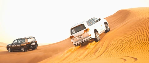 Dune bashing vehicles and camel silhouettes at golden hour in the Dubai desert