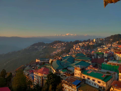The town of Darjeeling awakens in the golden light of sunrise, with the majestic, snow-capped Kanchenjunga range visible on the horizon
