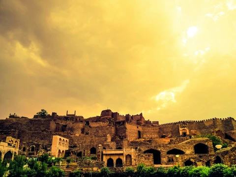 The Historic Golkonda Fort in Hyderabad, Telangana The ancient ruins and imposing stone ramparts of the Golkonda Fort stand on a hilltop under a dramatic, golden-tinted sky