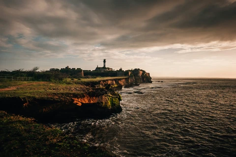 A Dramatic Sunset over the Historic Diu Fort The historic Diu Fort and its lighthouse stand on a rocky cliff overlooking the Arabian Sea under a moody, golden sunset sky