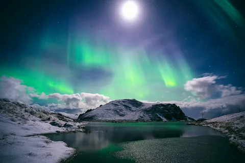 Auroras, Ice Caves & Black Sand: Iceland Northern Lights Tour | Safari Sutra Holidays Green northern lights over a snowy Icelandic mountain on an Iceland northern lights tour from India