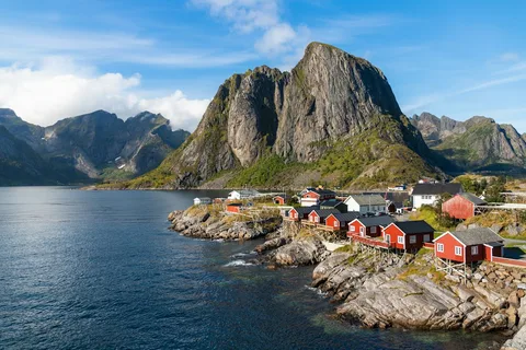Midnight Gold over Reine: Lofoten Photography Tour | Safari Sutra Holidays Red fishermen's cabins below jagged peaks in Reine on a Lofoten photography tour from India