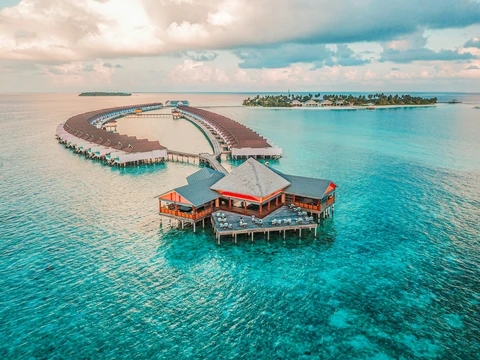 An aerial view of a luxury resort in the Maldives, showing a curved row of overwater villas in a stunning turquoise lagoon