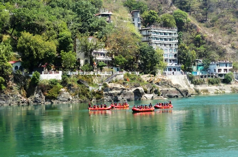 A group of tourists in red rafts enjoy a scenic river rafting trip on the calm, emerald green waters of the Ganges in Rishikesh