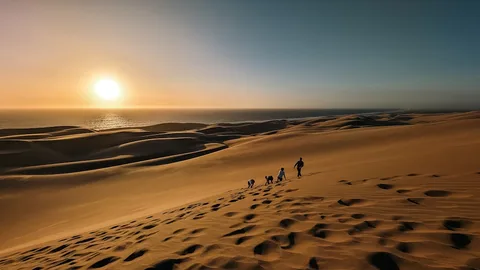 Namibia Honeymoon Escape | Safari Sutra Holidays Couple silhouetted on Namibia sand dune at sunrise — romantic honeymoon safari package from India