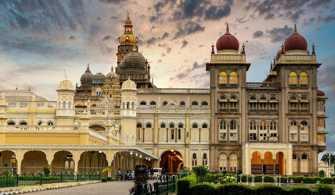The grand Mysore Palace in Mysuru, with its ornate domes and arches glowing under a dramatic evening sky
