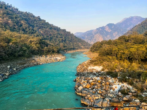 The Turquoise Waters of the Ganges River in Rishikesh The sacred Ganges River, with its stunning turquoise-colored water, flowing through the rocky, forested hills of Rishikesh