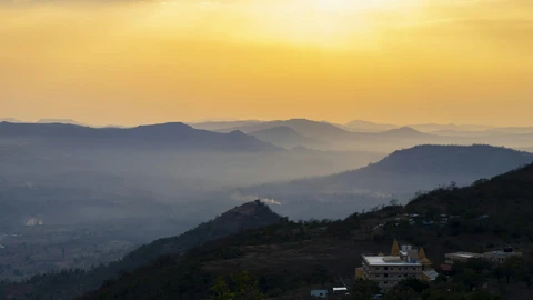 A panoramic sunset view from Bhandardara, showing layers of the Sahyadri mountains fading into a hazy, mist-filled valley