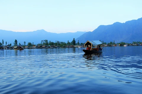 An Evening Shikara Ride on Dal Lake, Kashmir A Shikara boat floats on the calm, blue waters of Dal Lake at dusk, with the silhouettes of mountains in the background