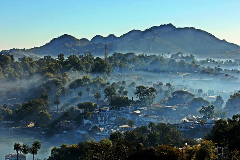 A Misty Morning in Mount Abu, Rajasthan A scenic view of the Mount Abu hill station, with the town and trees covered in a thick layer of morning mist and fog
